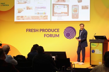 A man is giving a presentation on stage at the Fresh Produce Forum during Fruit Logistica in front of an audience.