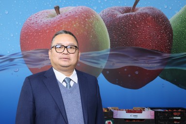 An Asian-looking man is standing in front of a wall on which a large apple can be seen.