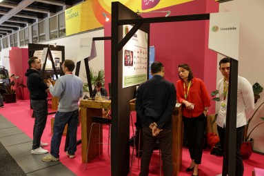 Startup Day 2024: Young entrepreneurs and trade visitors exchange ideas at exhibition stands on a pink carpet.