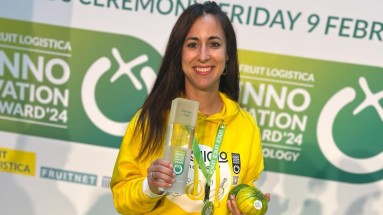 A woman in yellow hoody holds a trophy and a product while standing onstage.