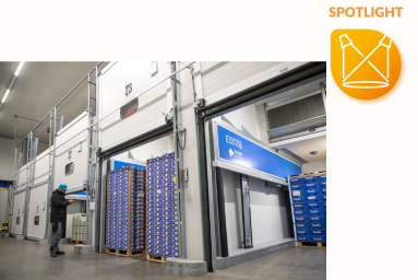 Cool boxes with open gates can be seen in a hall. There are pallets of fruit in the boxes and a man is checking them.