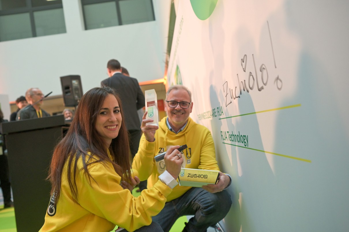 Two people in yellow hoodies kneel in front of a wall with products in their hands while writing ’Zucchiolo’ on the wall. They are smiling and taking part in an award ceremony.