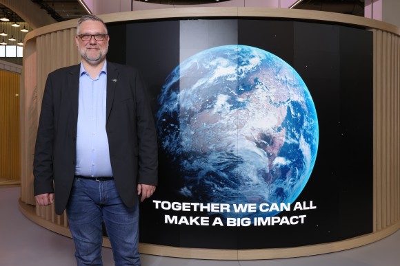 A man stands in front of a large picture with the earth on it and looks friendly into the camera. 