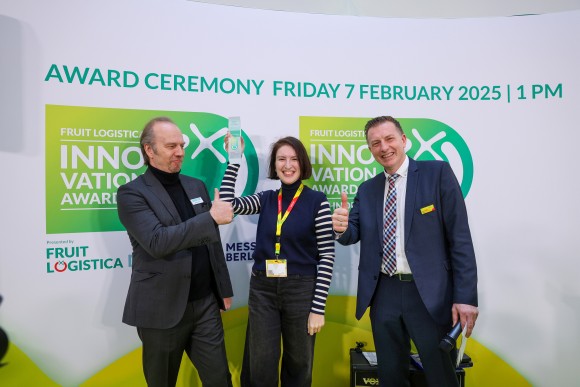 Three people stand smiling in front of a wall, holding a trophy in their hands. 