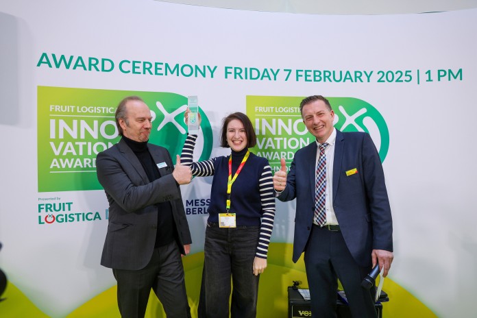 Three people stand smiling in front of a wall, holding a trophy in their hands. 